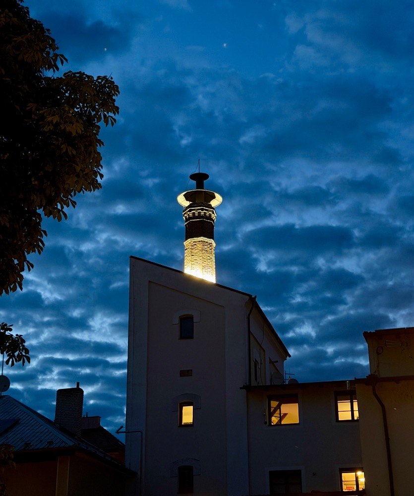 Nasvícený komín Poděbradského pivovaru za soumraku